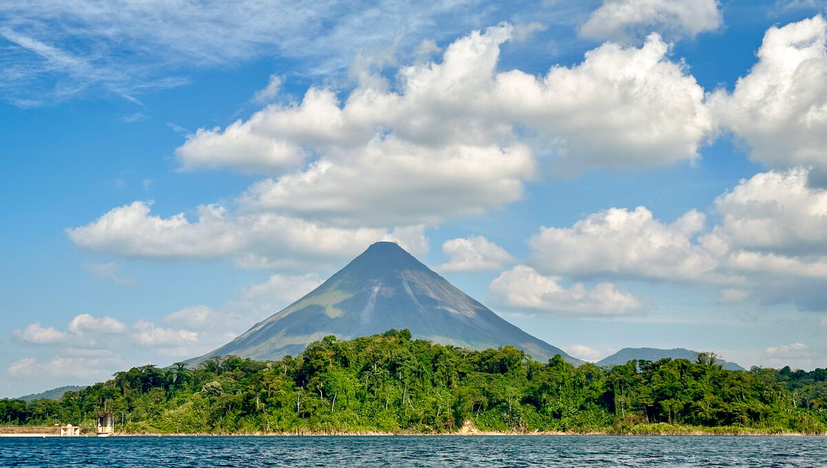 A volcano in the distance, with a jungle and a lake in front of it and big fluffy clouds behind it.